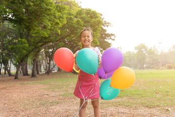 Happy little asian girl playing colorful balloons outdoors. Trees and green gardens background. Smiling lovely girl with balloons on the street in the summer. freedom and imagination concept.