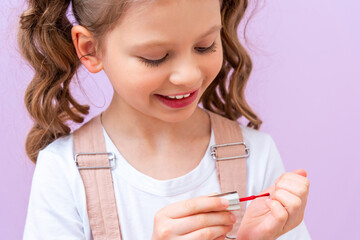 A little girl paints her nails with nail polish, a beautiful girl puts nail polish on her nails.