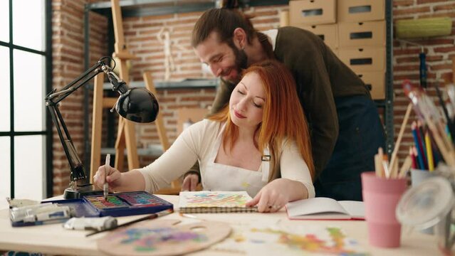 Man and woman artist couple hugging each other drawing on notebook at art studio