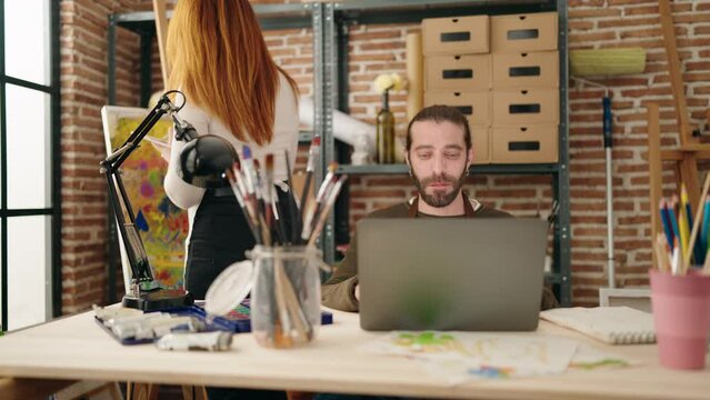 Man and woman artist couple using laptop painting nose at art studio
