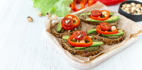 Vegan sandwiches with peppers, avocados, spicy spinach sauce and grain bread on a wooden tray and ingredients nearby. Side view, close-up. a light healthy snack. Dietary nutrition. Banner