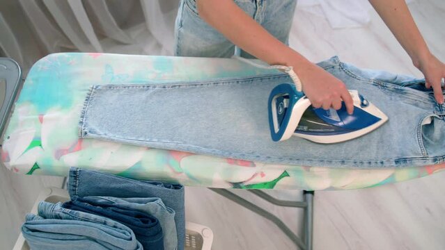 A young girl irons clean clothes on an ironing board with an iron in the room close-up. A woman's hand holds a hot iron around steam. The maid works with clothes, irons them and puts them in a basket.