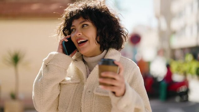 Young hispanic woman talking on the smartphone drinking coffee at street