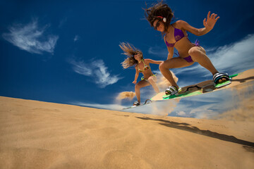 Kitesurf girls jumping on sandy beach with their arms raised against blue sky