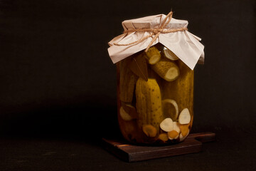 A glass jar with pickled cucumbers on a wooden stand