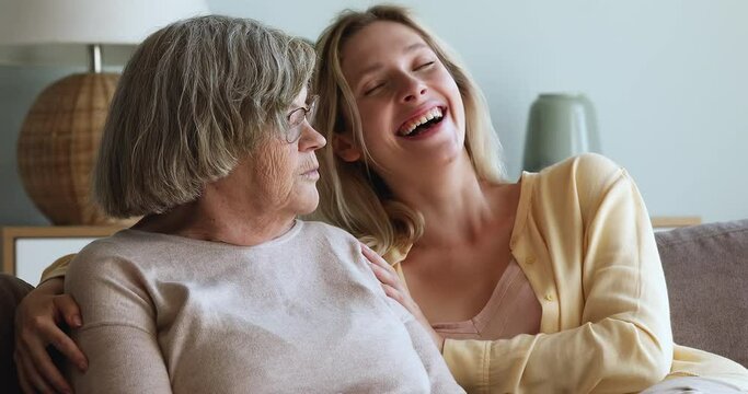 Close up cheery young adult granddaughter sit on sofa with 80s granny laughing enjoy pleasant conversation, multi generational women spend time together. Good warm relations, family bond, fun concept