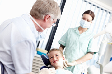 Fototapeta na wymiar Dental treatment clinic. Portrait of young boy smiling at dentist with assistant in office.