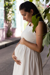 hermosa mujer embarazada latina, piel morena, ojos marrones, pelo oscuro. En un vestido blanco caminando por las coloridas calles de Cartagena, Colombia. enfoque suave