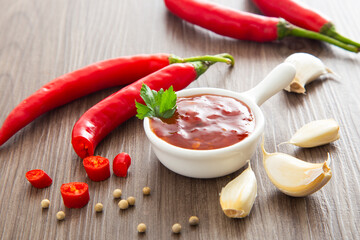 Bowl of hot chili sauce with red peppers on dark wooden background,