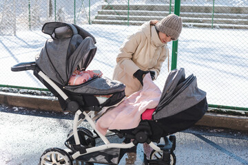 Mother tucking blanket for baby in stroller while sitting outside on park bench
