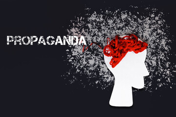 Paper silhouette of a head with red threads instead of brains on a black background. Flat lay. The concept of disinformation and propaganda - obrazy, fototapety, plakaty