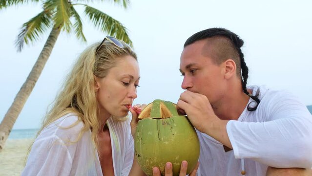 Sexy loving couple under a palm tree kissing, hugging and drinking coconat cocktail Pina Colada. Concept honeymoon relationship romance beach tropical tourism, summer wedding love family vacations