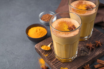 Immuno-supportive drink with milk, turmeric, coffee and cinnamon on a dark background. Latte with turmeric. Side view, close-up.