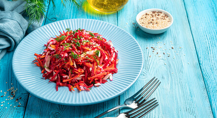 Summer vegetable salad with cabbage, beets, carrots and sesame seeds on a blue background. Side view, space to copy.