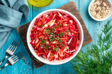 Vitamin vegetable salad with beets, carrots and cabbage in a white bowl on a blue background. Top view.