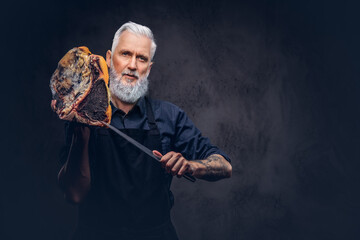 Bearded elderly butcher with knife and meat piece