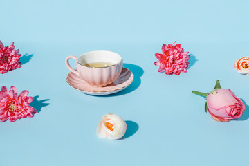 Creative layout with cute pink tea cup surrounded with fresh flowers and on pastel blue background....