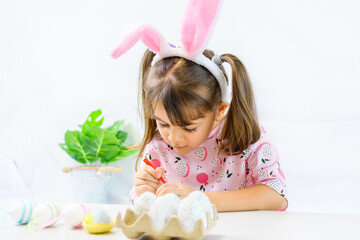 Happy little girl with bunny ears painting the egg with fiberpen, preparing for Happy Easter day. Preparing handmade .