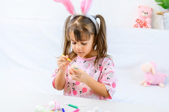 Happy little girl with bunny ears painting the egg with fiberpen, preparing for Happy Easter day. Preparing handmade .