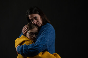 Sad mother hugging her daughter, both wearing Ukrainian national colors on black background.