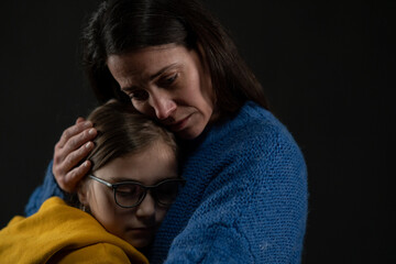 Sad mother hugging her daughter, both wearing Ukrainian national colors on black background.