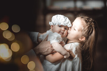 the elder sister kisses a baby in a baptismal outfit in a temple or church who came to worship in...