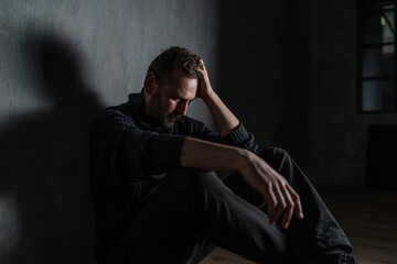 Sad mature man, alone in darkness, sitting and thinking.