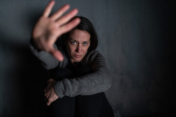 Depressed mid-adult woman, alone in darkness, looking at camera, stop the war concept.