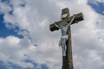 Crucified Jesus. Figure of Jesus Christ against the background of blue sky. Old, stone cross.