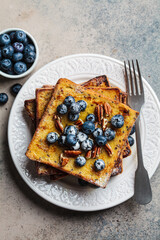 French toast with blueberries, pecan and maple syrup for breakfast on white plate.