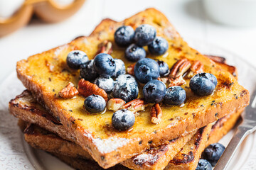 French toast with blueberries, pecan and maple syrup for breakfast on white plate.