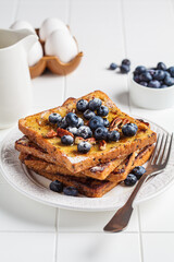 French toast with blueberries, pecan and maple syrup for breakfast on white plate.