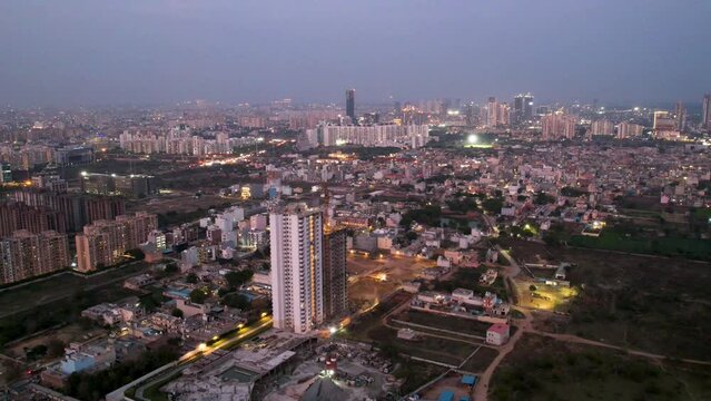 dusk to night aerial hyper lapse showing under construction tower with crane on top with traffic vehicle lights moving across in the distance showing the rapid development in Indian cities like Delhi