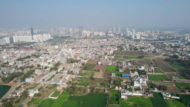 aerial panning shot showing densely populated houses, skyscrapers under construction, farms and feilds and a pond showing the scattered development of Indian cities like Gurgaon, Vijaywada, kolkata