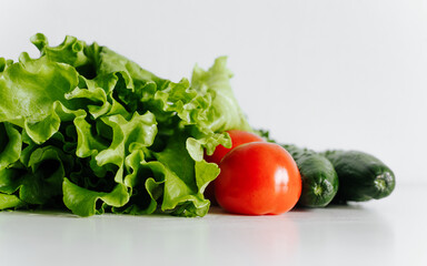 Greens, healthy eco food concept. Close-up eco friendly organic food, fresh vegetables. Lettuce, cucumbers, tomatoes on white kitchen table indoors. Selective focus