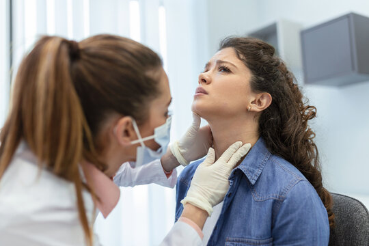 medicine, healthcare and medical exam concept - doctor or nurse checking patient's tonsils at hospital. Endocrinologist examining throat of young woman in clinic
