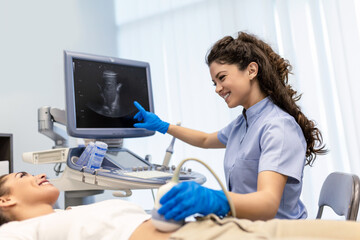 Obraz premium Ultrasound diagnostic of stomach on abdominal to woman in clinic, closeup view. Doctor runs ultrasound sensor over patient's girl tummy and looks at image on screen. Diagnosis of internal organs.