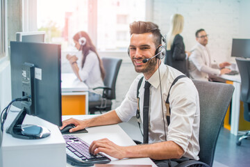 Handsome male call center operator in headset working in modern office. Hotline support service concept - obrazy, fototapety, plakaty