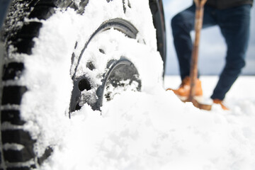 man digging car wheels from the snow with shovel
