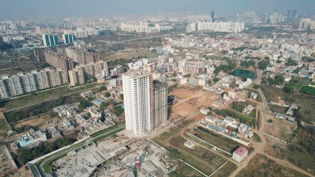 aerial orbiting shot of under construction skyscraper with crane on top and densely populated houses all around showing property, infrastructure development and real estate in key cities