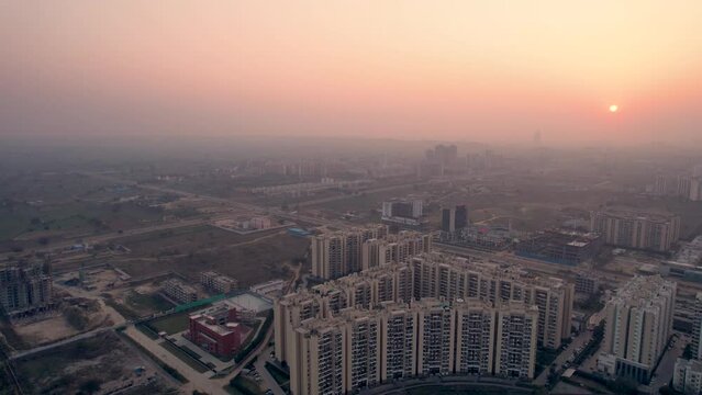 flying towards aerial drone shot showing dust, fog, smog covered city at sunset dusk with crecent shaped apartment buildings stretching out into the distance showing population density in Indian