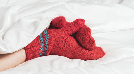 Womens hands in red mittens on white blanket. The warmth of home comfort.