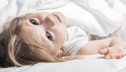 Little girl under white blanket. The warmth of home comfort.