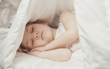 Little girl sleeps under white blanket. The warmth of home comfort.