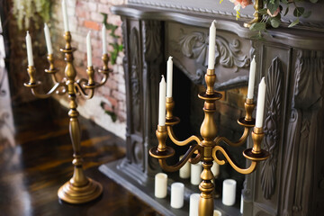 White candles in elegant gilded candlesticks near the fireplace in the room