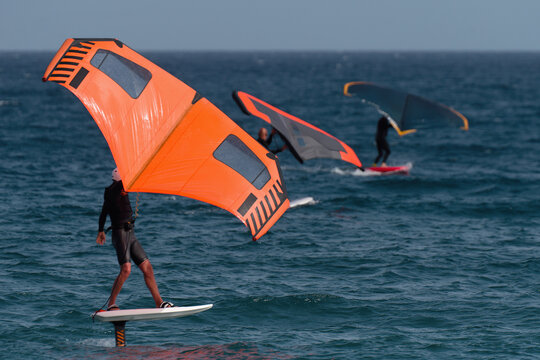 A Group Is Wing Foiling Using Handheld Inflatable Wings And Hydrofoil Surfboards In A Blue Ocean, Rider On A Wind Wing Board, Surf The Waves