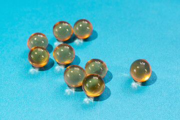 Yellow round capsules with fish oil for nutrition omega diet health benefits close-up on a blue background with copy space
