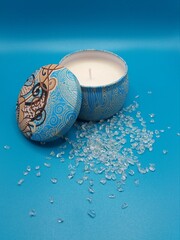 Candle in decorative tin with lid with a blue background and broken glass