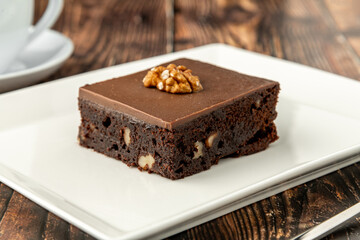 Walnut and dark chocolate brownie on a white porcelain plate on wooden table