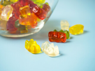 Bowl with tasty bright gummy bears on blue table